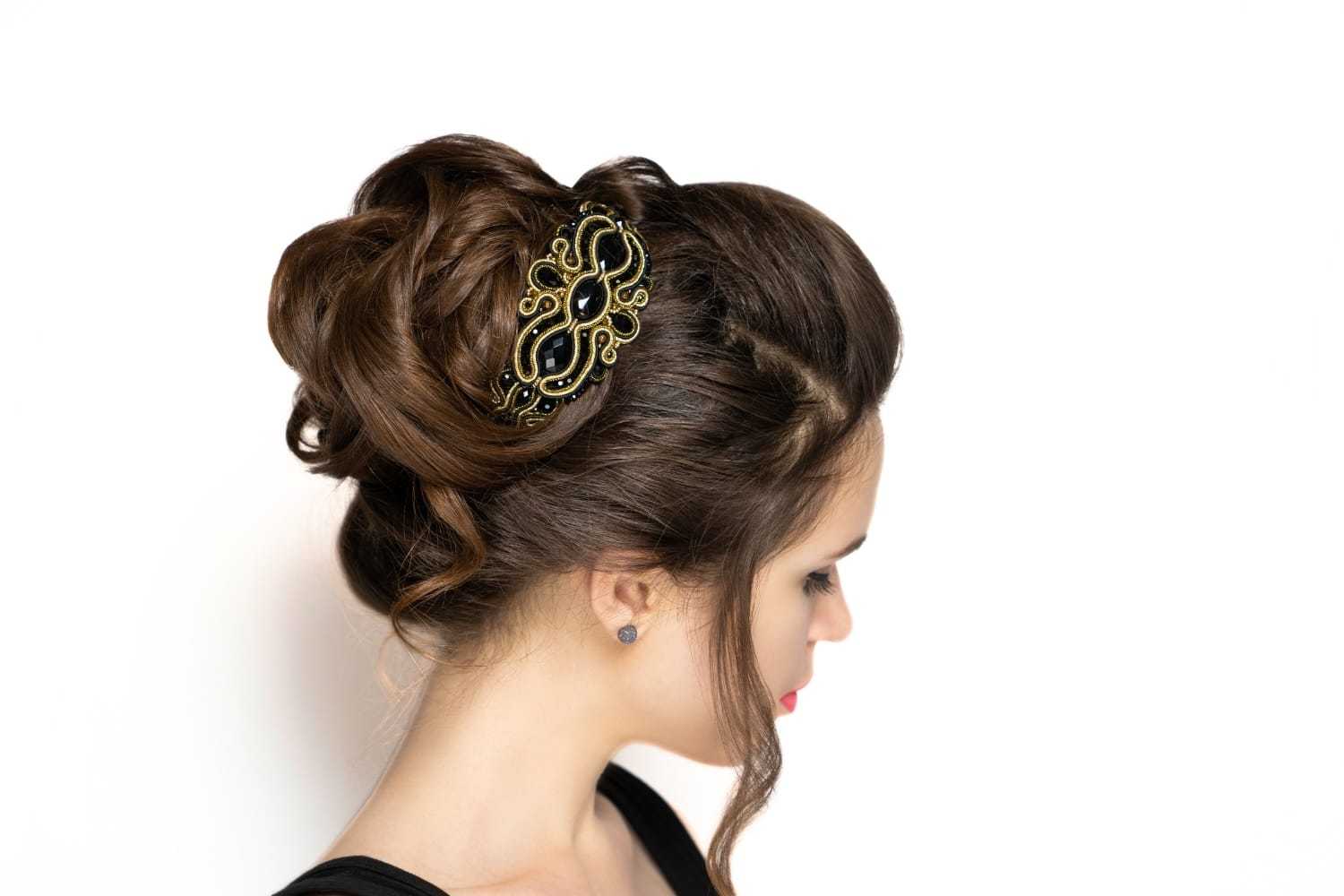 Woman with an elegant updo hairstyle adorned with an intricate hair accessory, facing sideways.