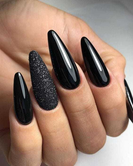 Close-up of manicured hand with long, glossy black nails, one covered in black glitter.