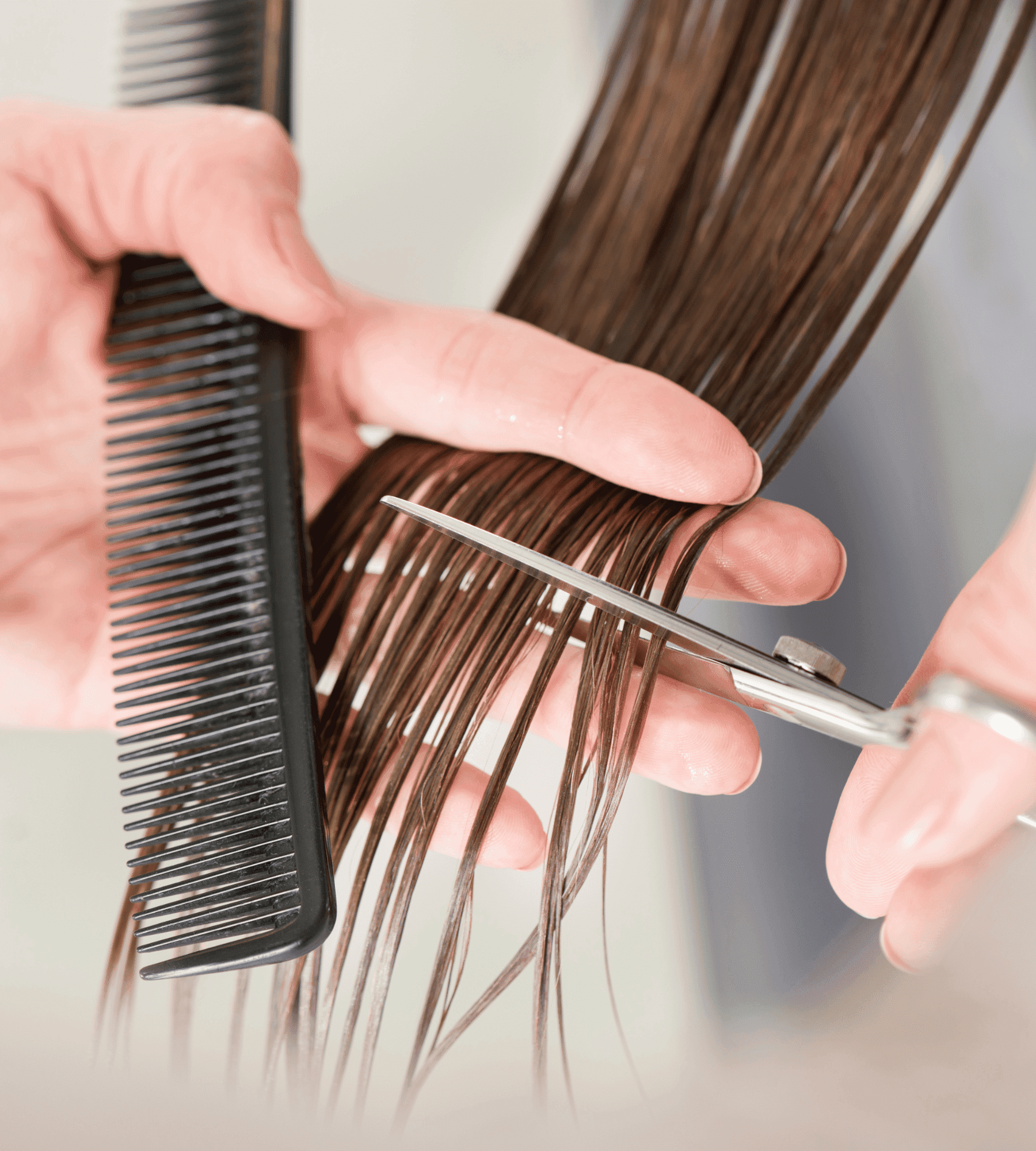 Close-up of hands cutting long brown hair with scissors and comb.