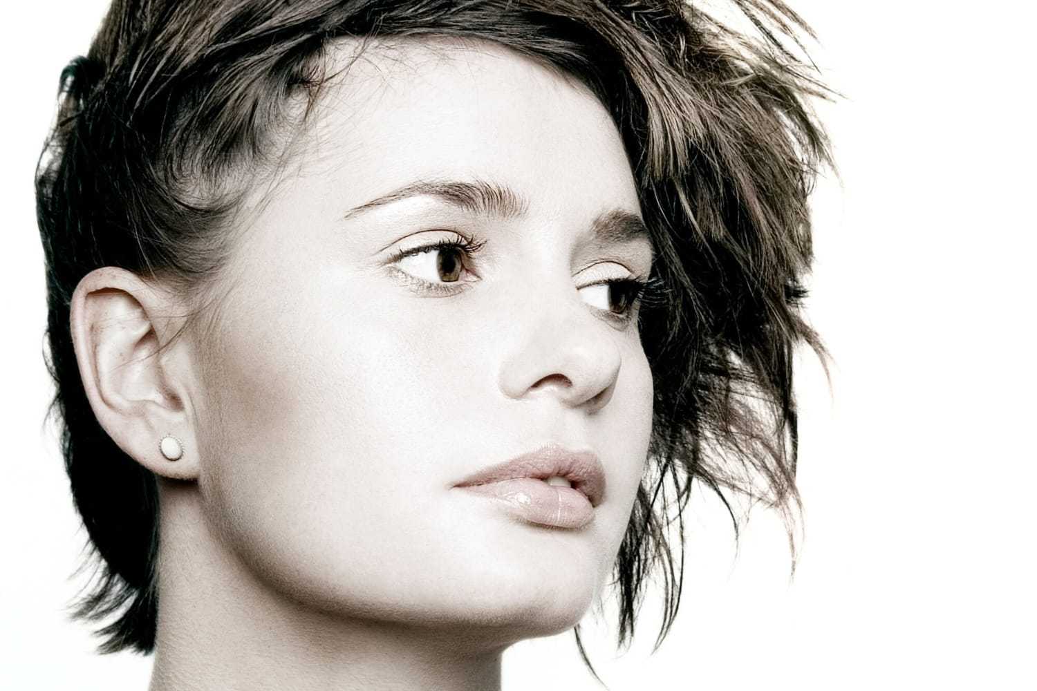 Portrait of a woman with short, tousled hair looking to the right against a white background.