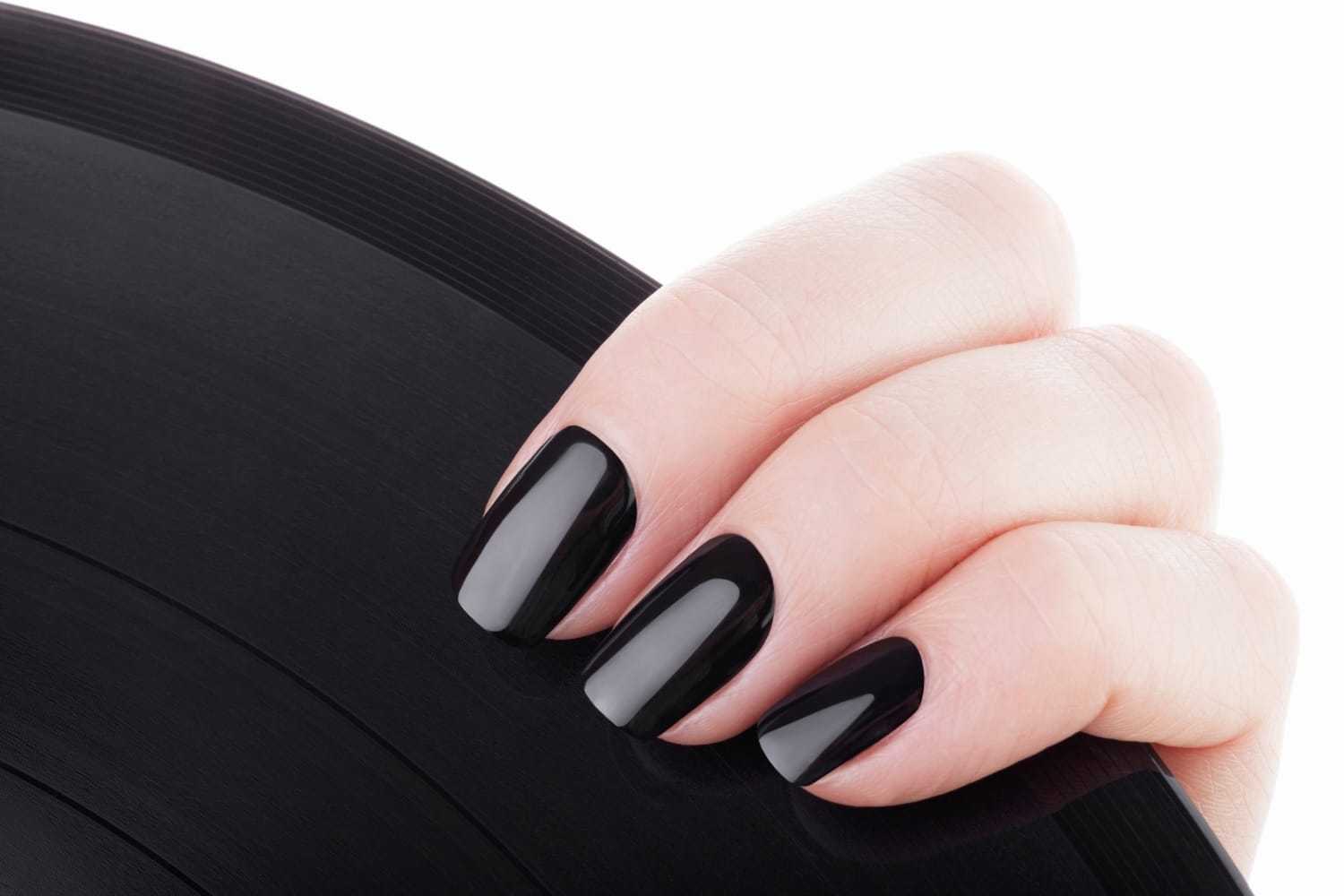 A hand with black-painted nails holding a black vinyl record against a white background.