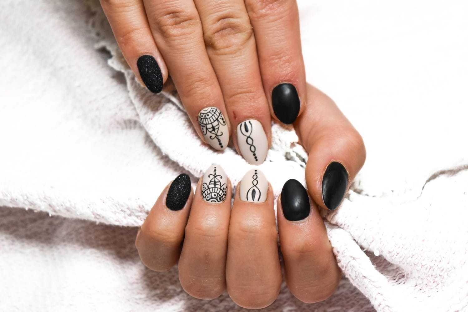 Hand with black and white intricately designed nails holding a textured white cloth.
